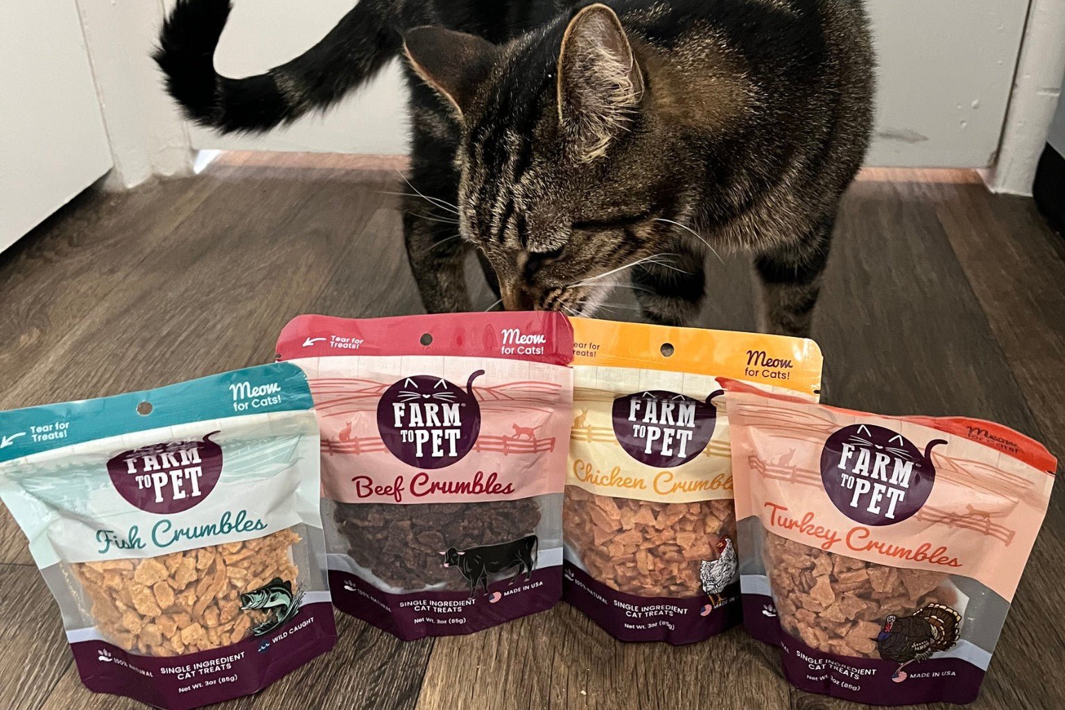 Tabby cat sniffing bags of Farmto-pettreats Crumbles cat treats.