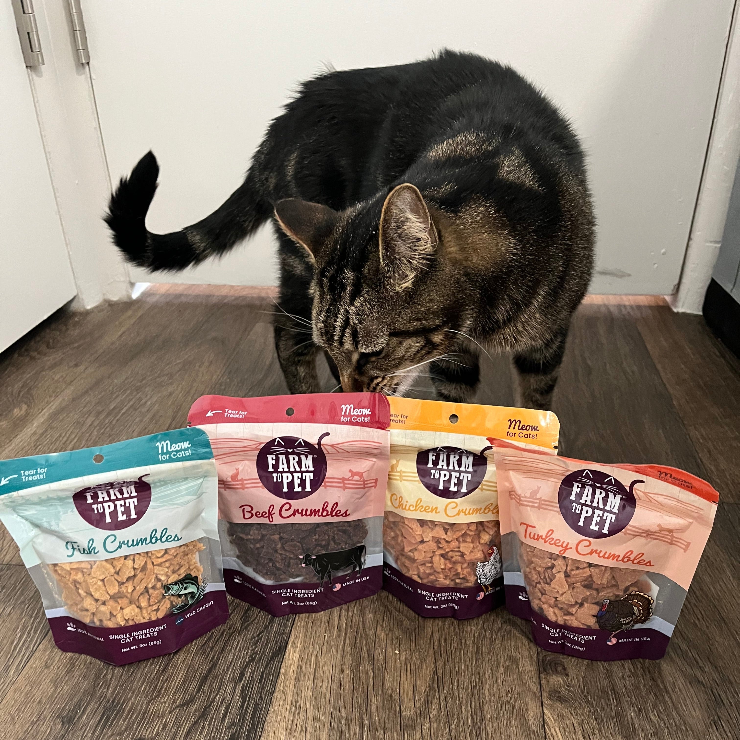 Cat looking at a row of Farmto-pettreats cat crumble packages on a wooden floor.