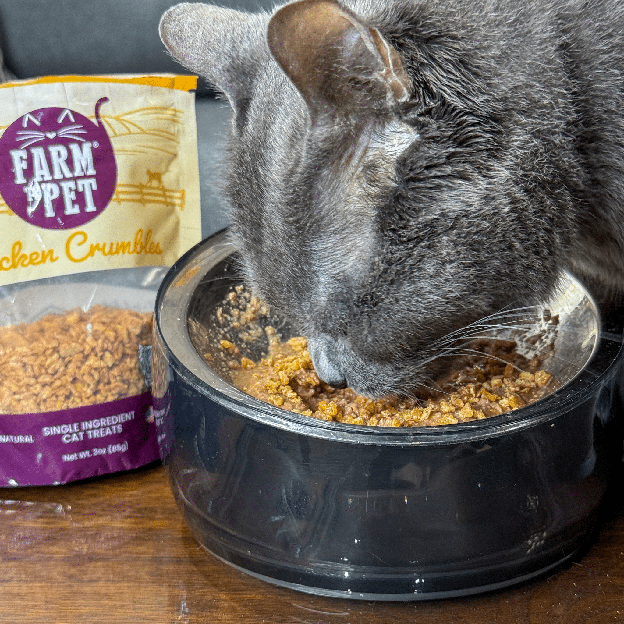 Product picture of Farmto-pettreats Chicken Crumbles with a gray cat eating from a bowl. 