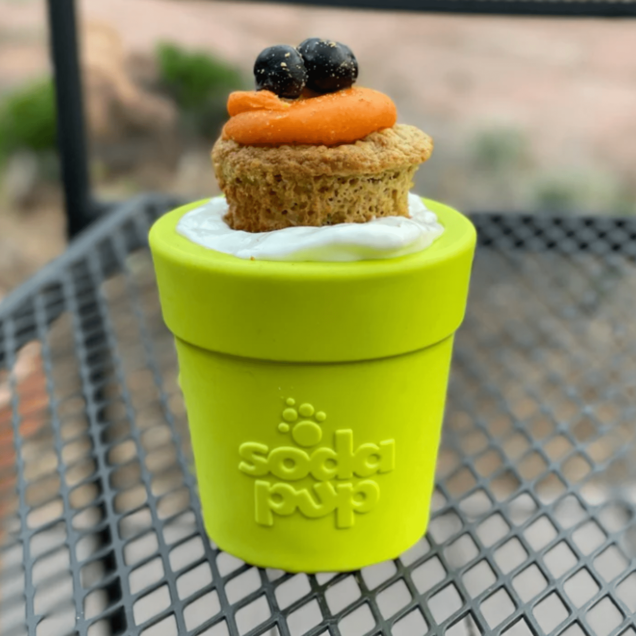 Farmto-pettreats Dog Food Dispenser a Green Flower pot with a small cupcake on top, sitting on a metal surface.