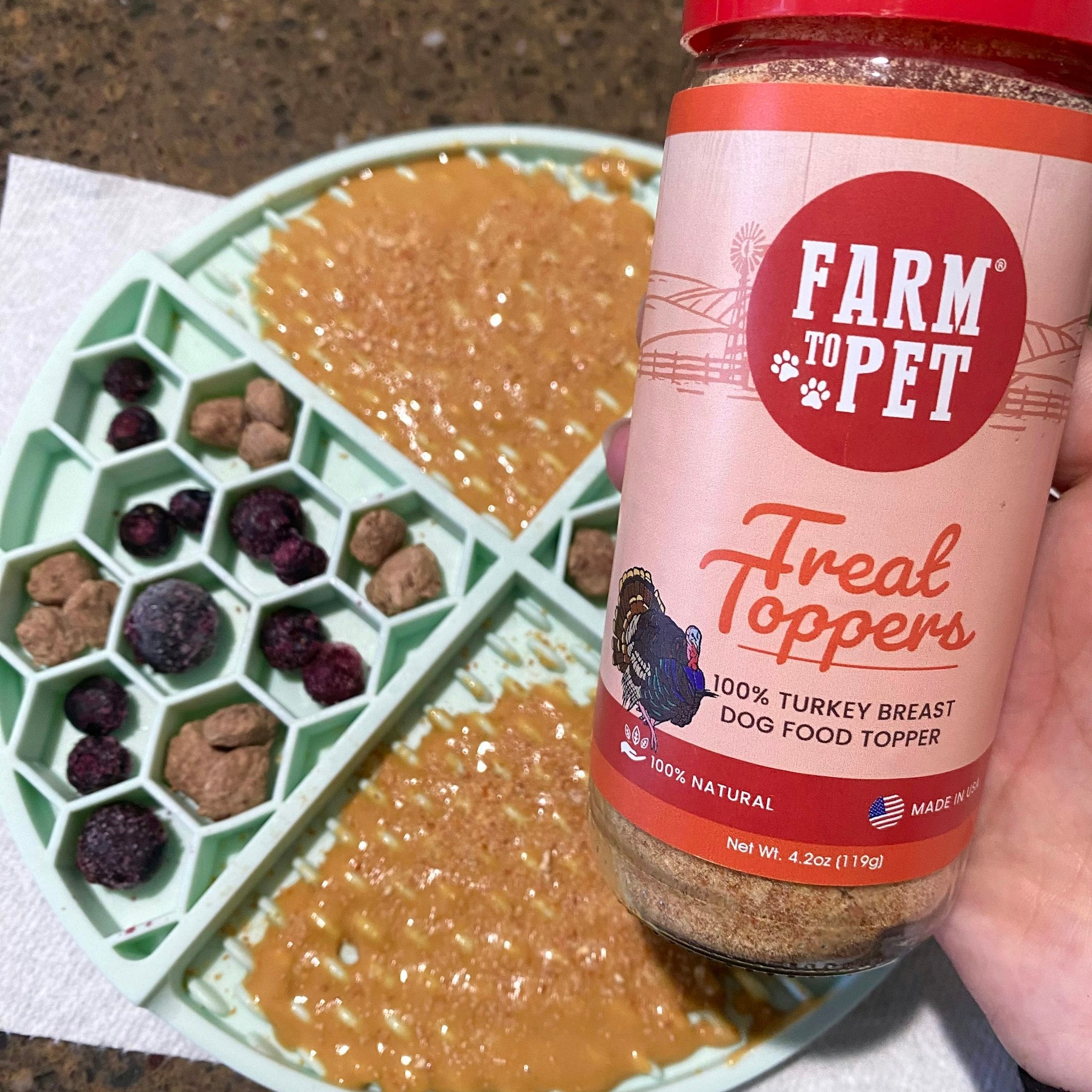  A green lickmat sprinkled with a jar of Farmto-pettreats Turkey Treat Dog Food Topper.