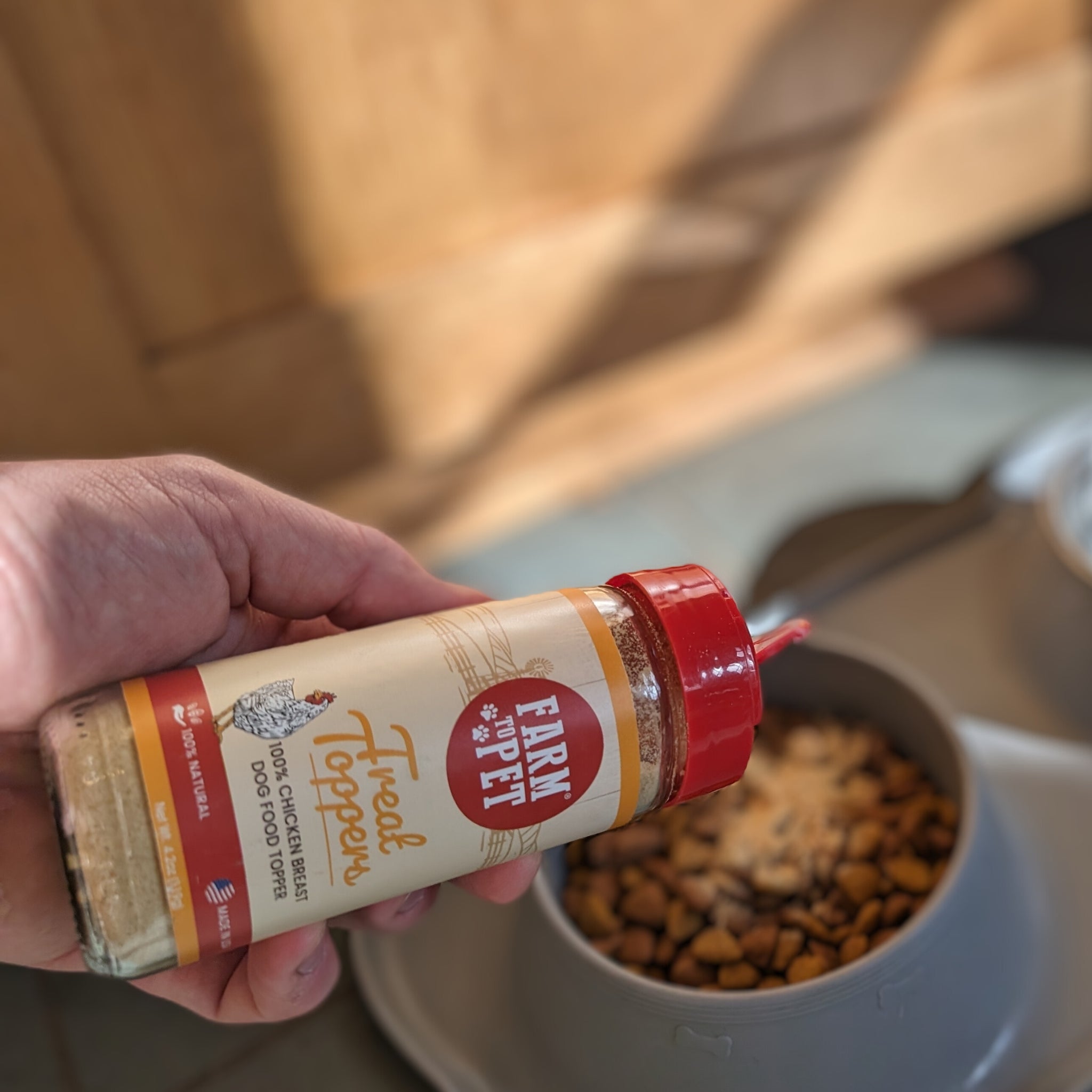 A jar of Farmto-pettreats Chicken Topper sprinkled on a bowl of dog food.