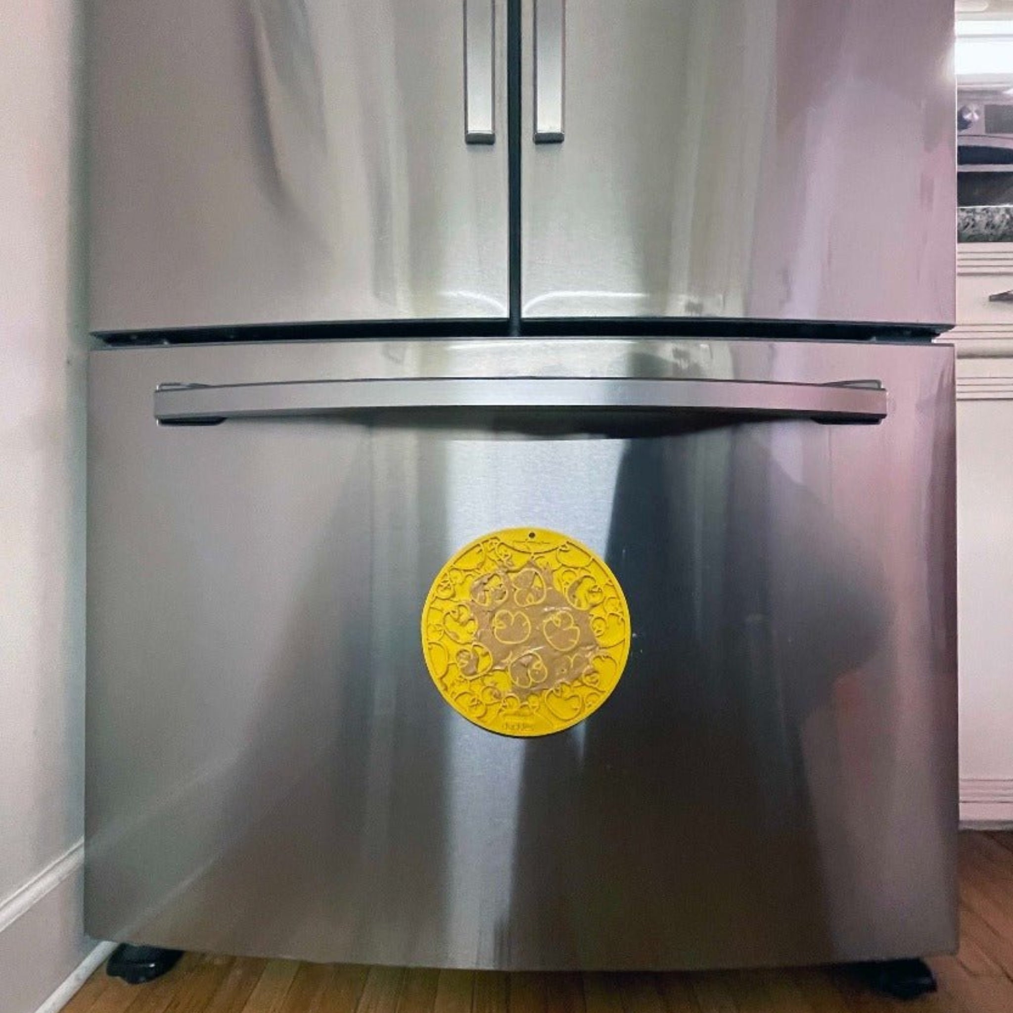 A Farmto-pettreats and Sodapup Yellow Duck Lick Mat suctioned to a bottom of  a Stainless steel refrigerator.