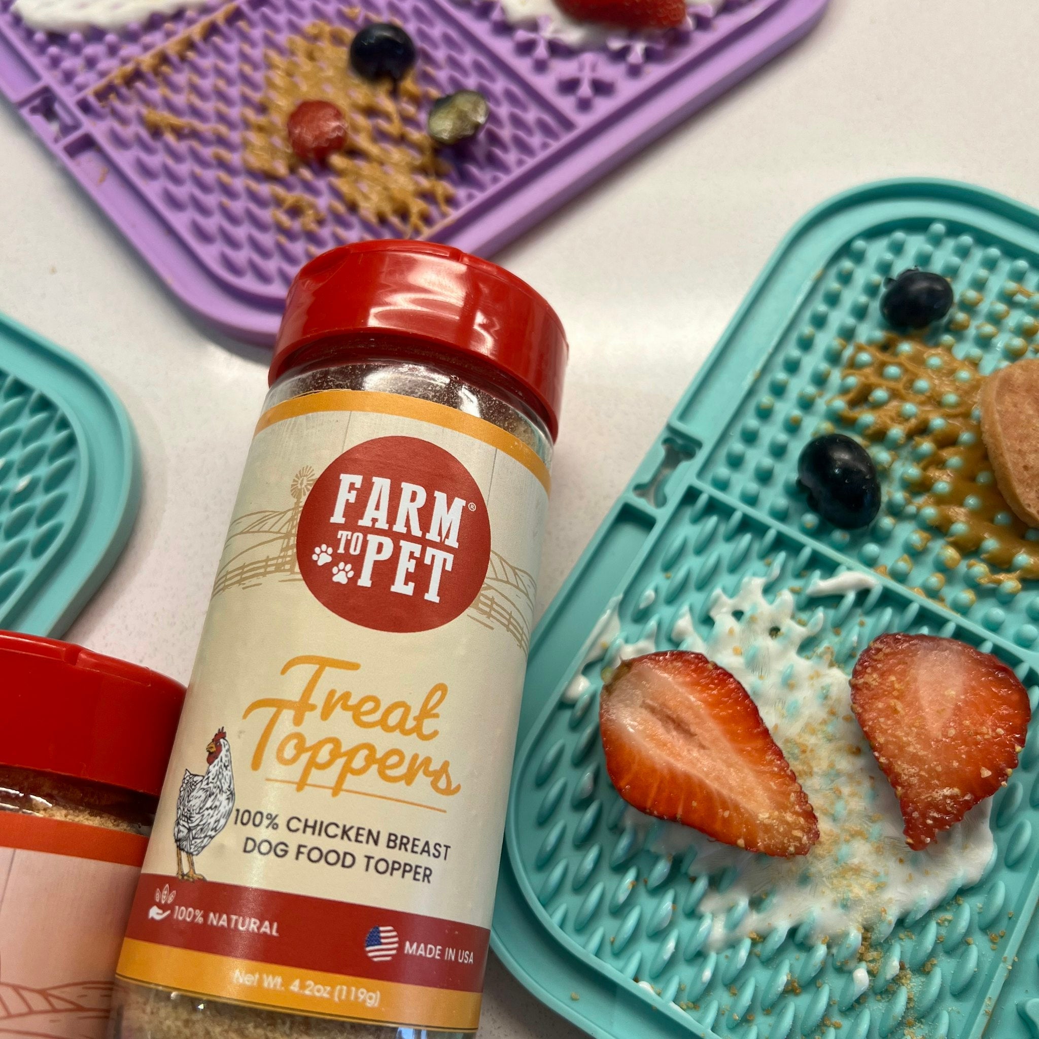 Farmto-pettreats Chicken Treat Dog Food Topper in a purple and light blue lick mats with strawberries in it sprinkled with our chicken toppers.